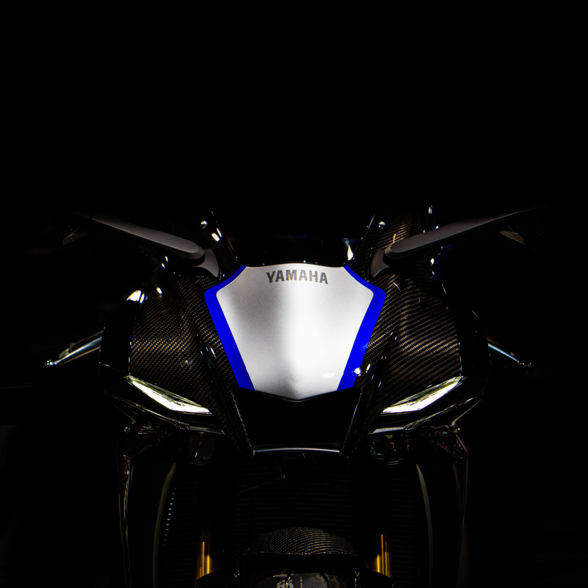 Schmale Frontverkleidung einer blau-weissen Yamaha R1 mit Carbon-Elementen. Die beiden flachen LED-Scheinwerfer unter dem «Yamaha»-Schriftzug wirken wie zusammengekniffene Augen.