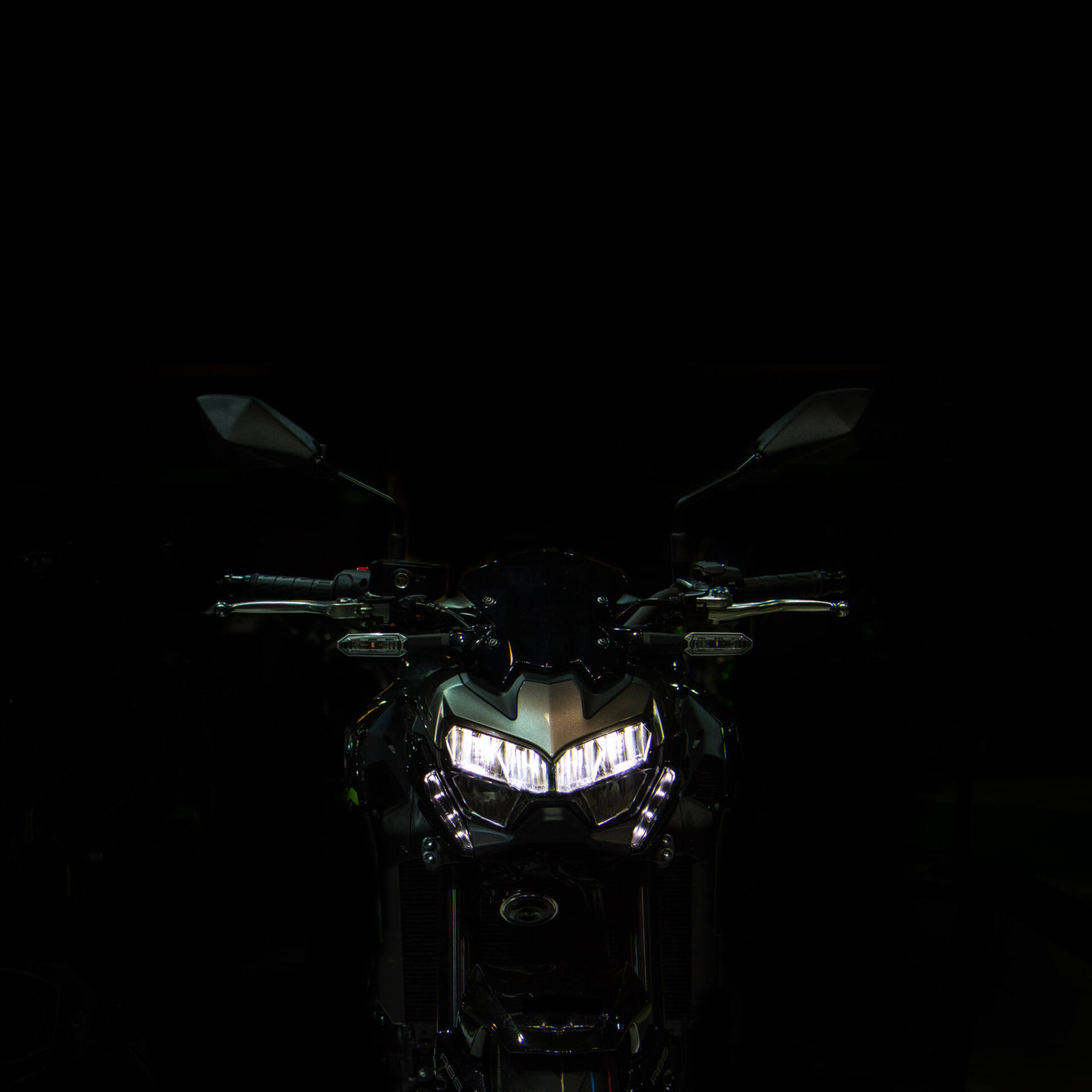 Front eines grau-schwarzen Kawasaki-Nakedbikes im Dunkeln. Der schmale, scharf geschnittene LED-Scheinwerfer wirkt wie ein Paar zusammengekniffener Augen zwischen Lenker und Spiegeln.