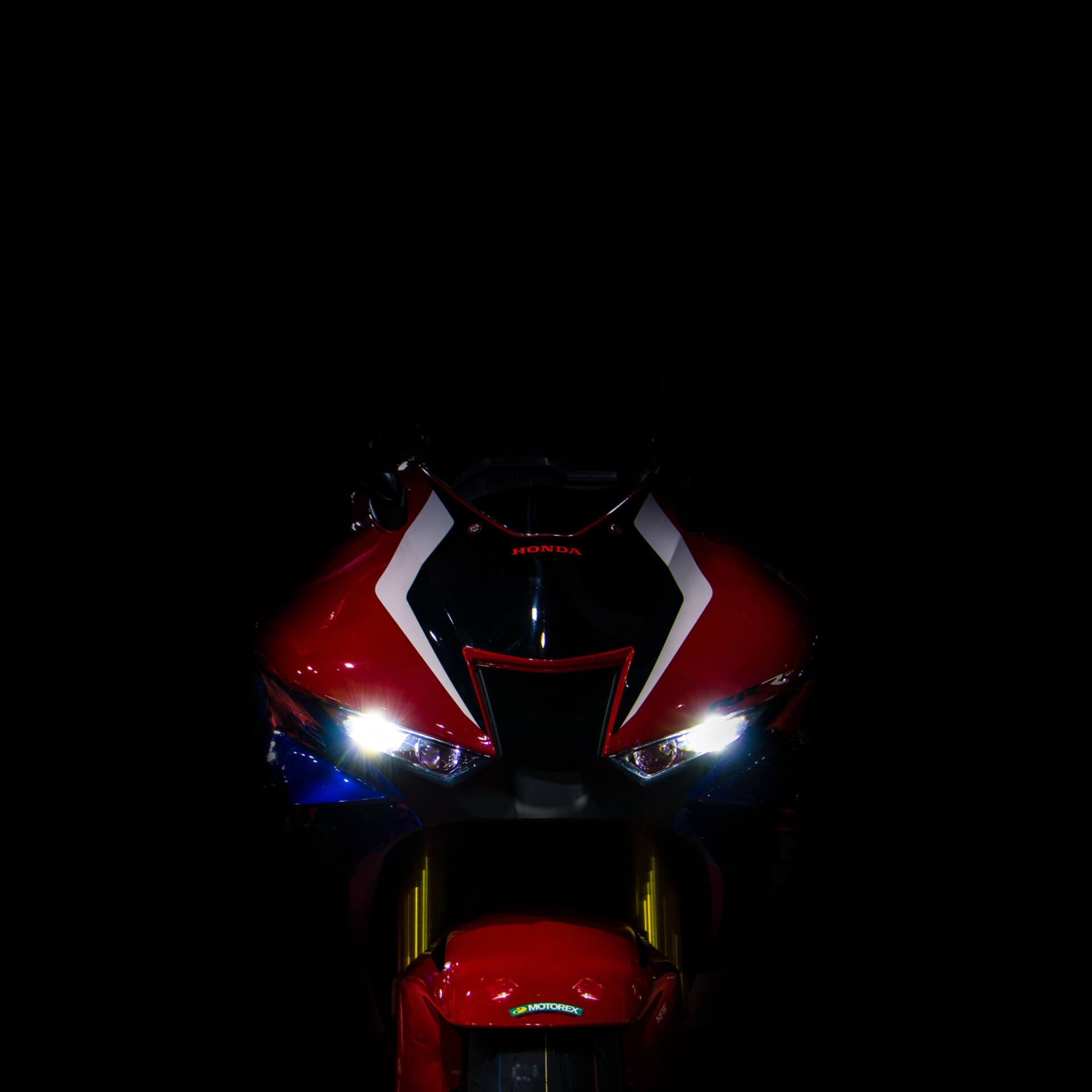 Front einer rot-weiss-blauen Honda Fireblade im Dunkeln. Die beiden hell leuchtenden LED-Scheinwerfer links und rechts der Lufthutze wirken wie ein schmales, fokussiertes Renngesicht.