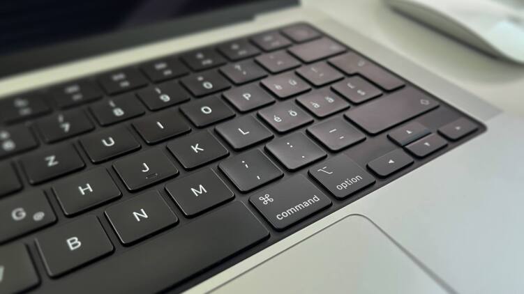 Nahaufnahme der schwarzen Tastatur eines MacBook mit Schweizer Layout, im Vordergrund die Tasten Command, Option und die Komma-Taste.